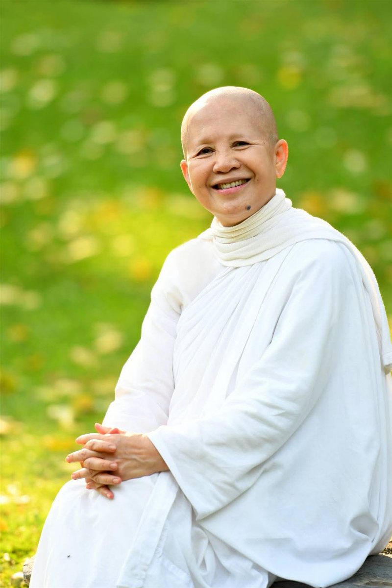 Ven. Mae Chee Sansanee Sthirasuta, smiling, seated outdoors in white robes